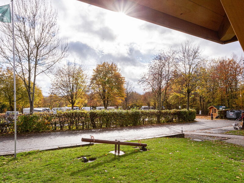 Ein Spielplatz mit Wippe im Vordergrund und Wohnmobilen im Hintergrund an einem sonnigen Herbsttag