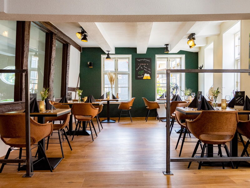 Ein Restaurant mit braunen Ledersesseln, Holztischen und schwarzer Tischwäsche, beleuchtet von