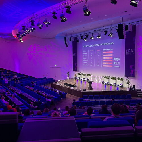 Eine Frau hält einen Vortrag auf einer Bühne vor einem Publikum in einem großen Saal