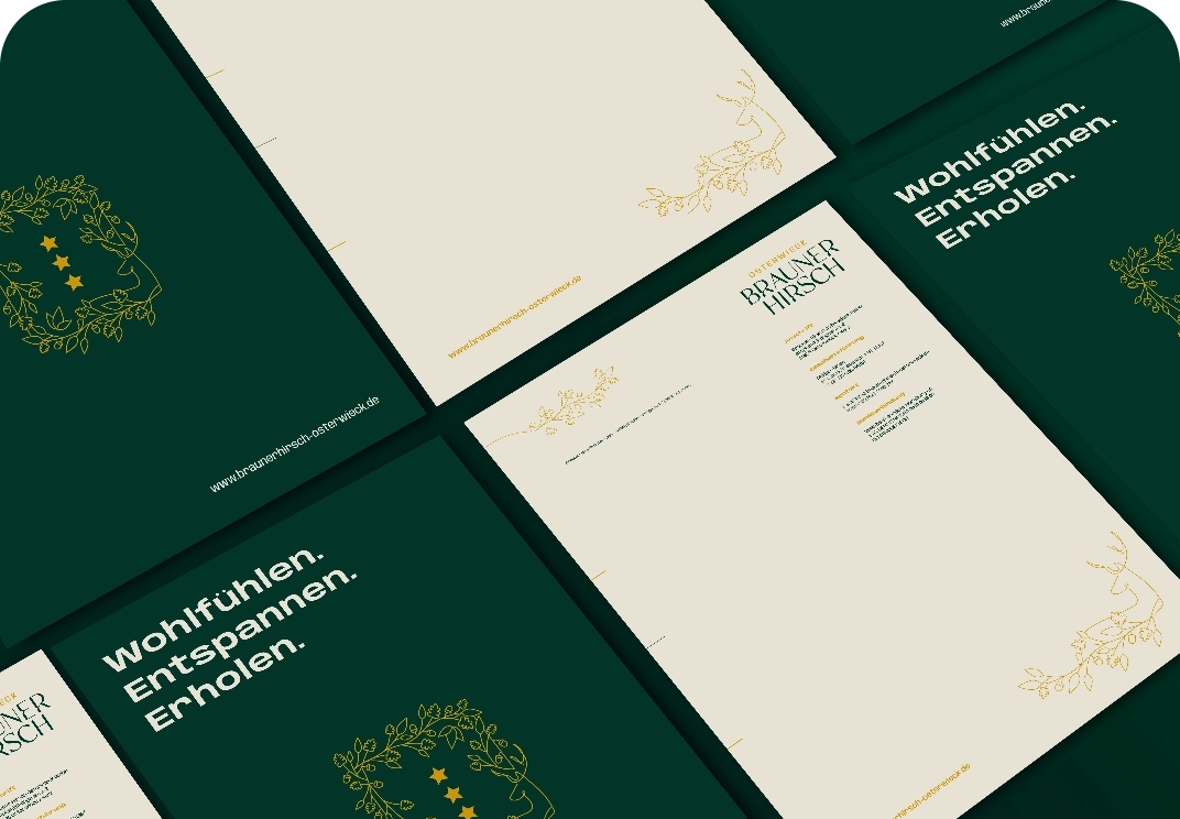 Beigefarbene Geschäftspapiere mit goldenen Ornamenten und dem Logo Brauner Hirsch liegen auf dunkelgrünem