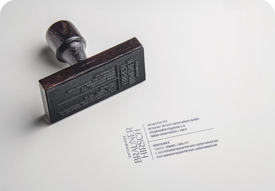 Stempel mit Holzgriff und eingeprägtem Firmenlogo von Brauner Hirsch Osterwieck GmbH, daneben Kontaktdaten auf