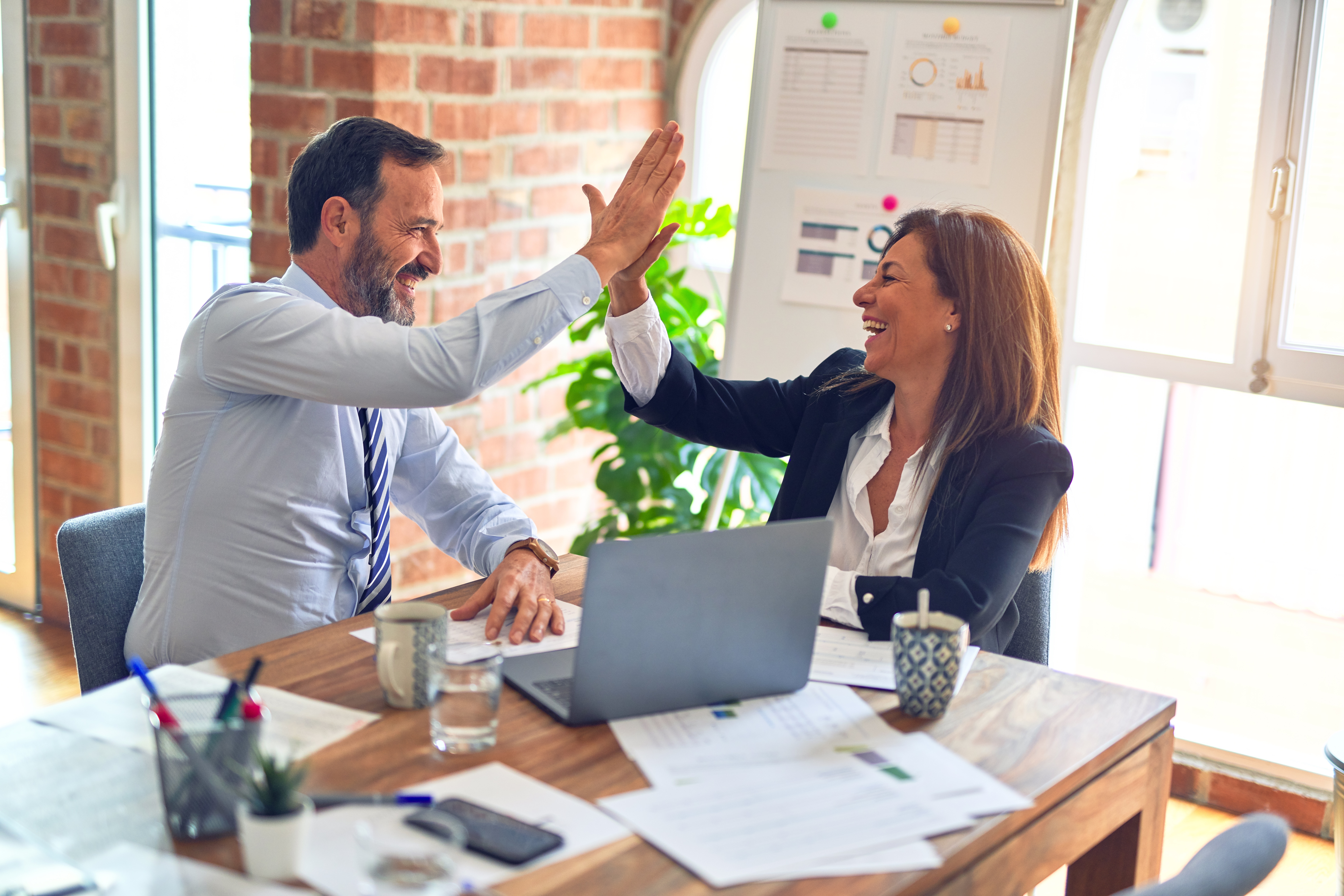 Ein Mann und eine Frau geben sich im Büro die High Five über einen Schreibtisch