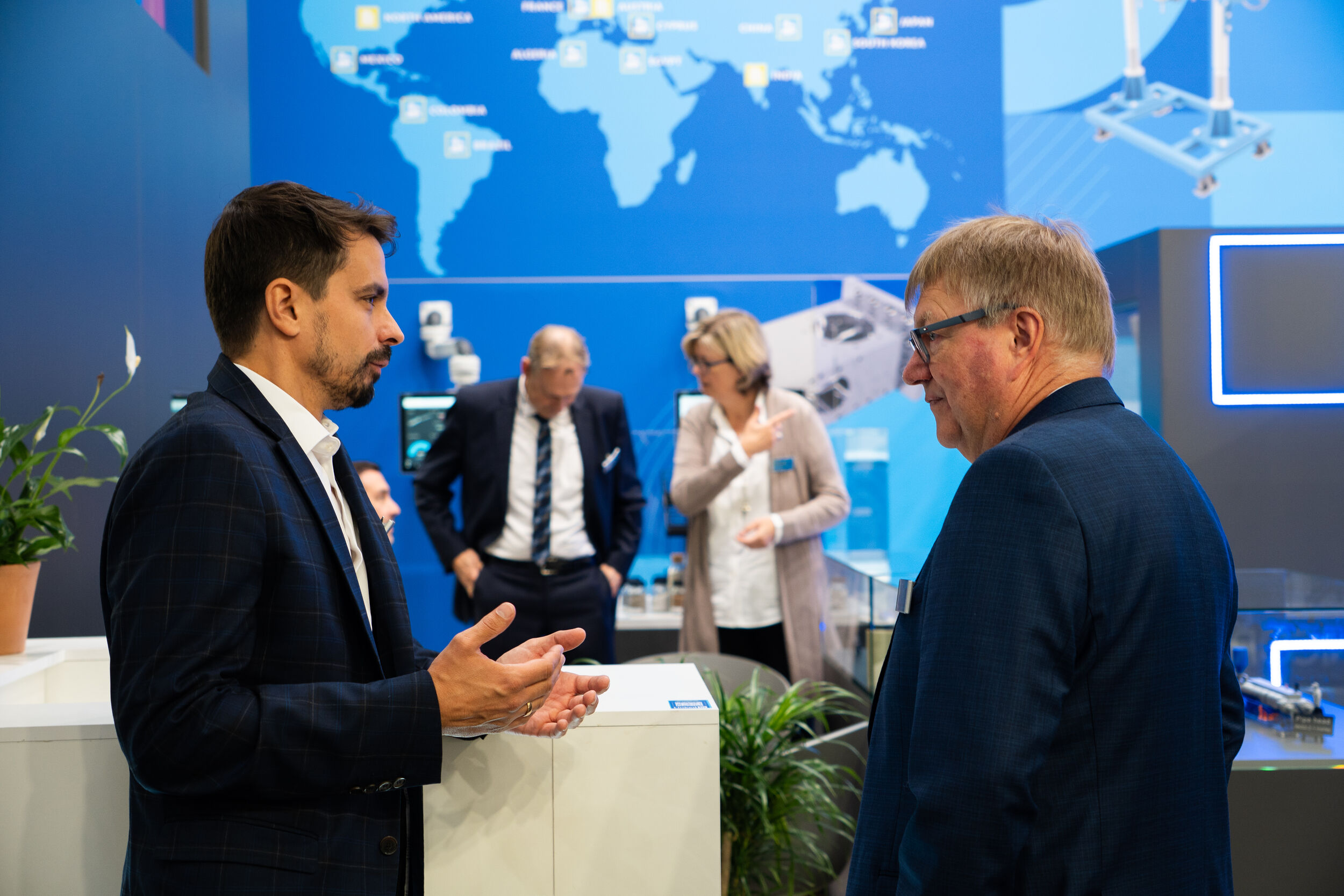 Profilansicht zweier Gesprächspartner vor Theysohn Extrusionstechnik GmbH Messestand